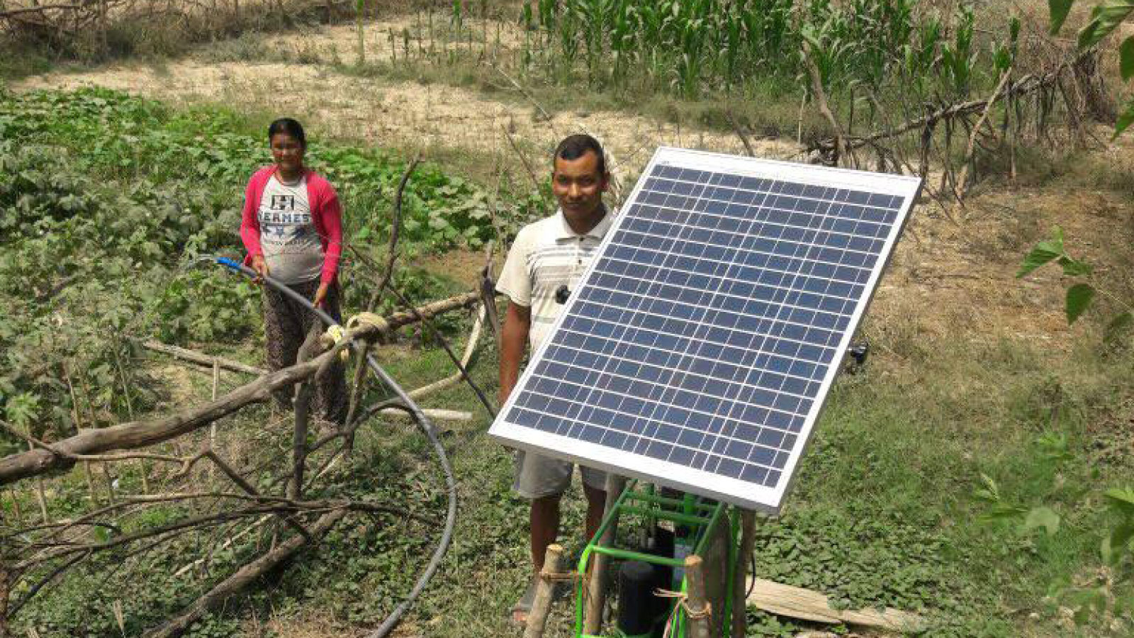 Two farmers in Nepal stand with their solar irrigation pump and irrigate the land behind