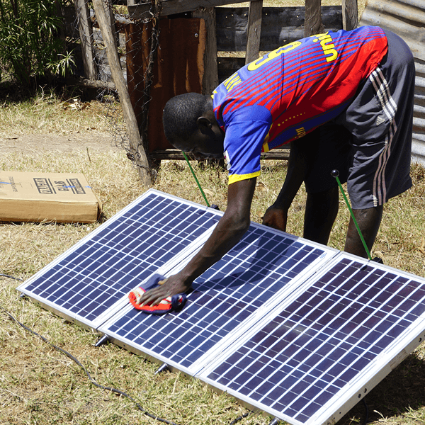 A man bending to wipe the dust off sun panels so that they work efficiently.