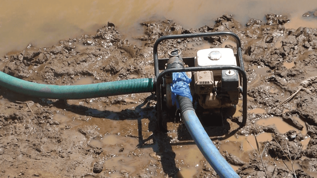 An image of a black petrol pump in muddy, wet earth. The blue hosepipe has a bag wrapped around it where it attaches to the pump, clearly an attempt to fix a leak. This is not a long-lasting agricultural product.