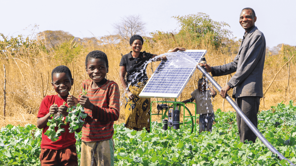 A family in Zambia standing with a Futurepump solar pump on a farm surrounded by crops