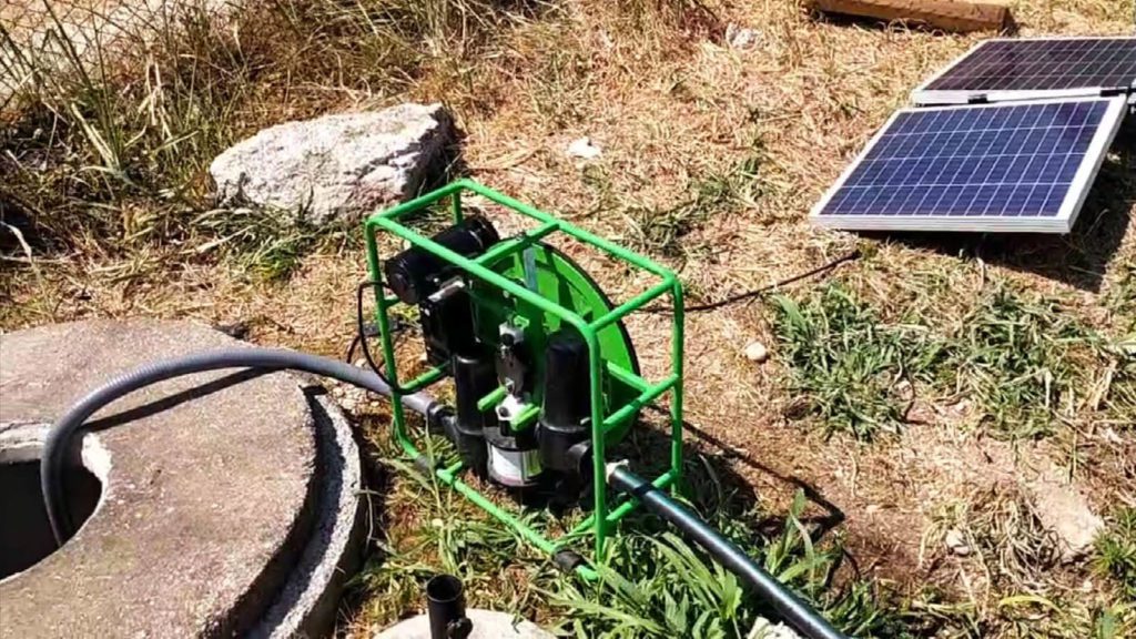 Treebù's SF2 solar water pump in a field. The water is being pumped from a well and the solar panels are shiny in the sunlight.