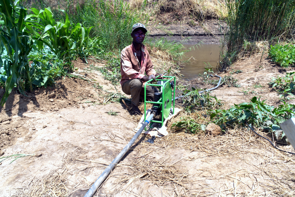 In the centre of the photo is a farmer sitting with his green Futurepump solar pump. It has a pipe running down into the river behind him